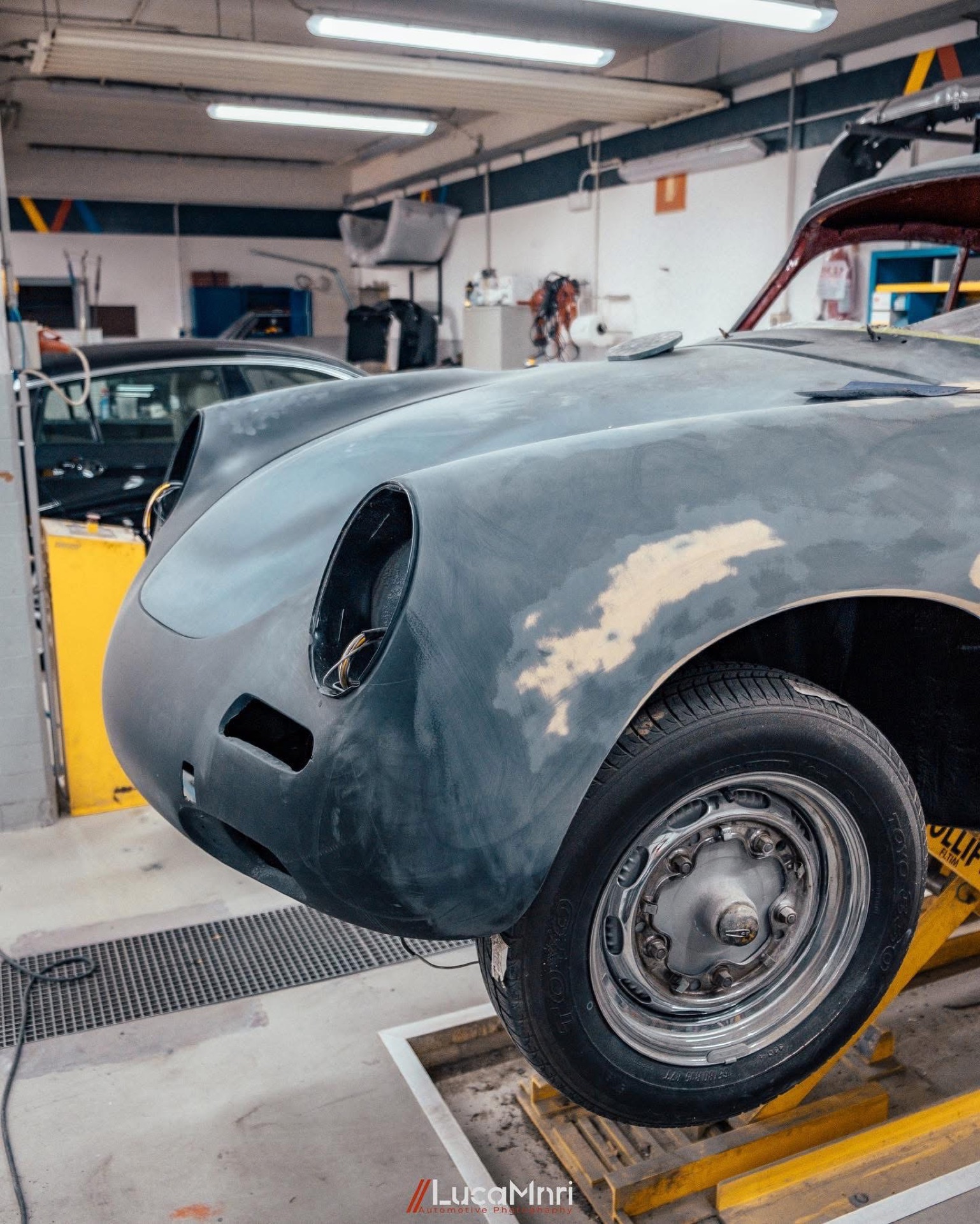Frontale ravvicinato di una Porsche 356 in restauro, senza fari e in fondo grigio